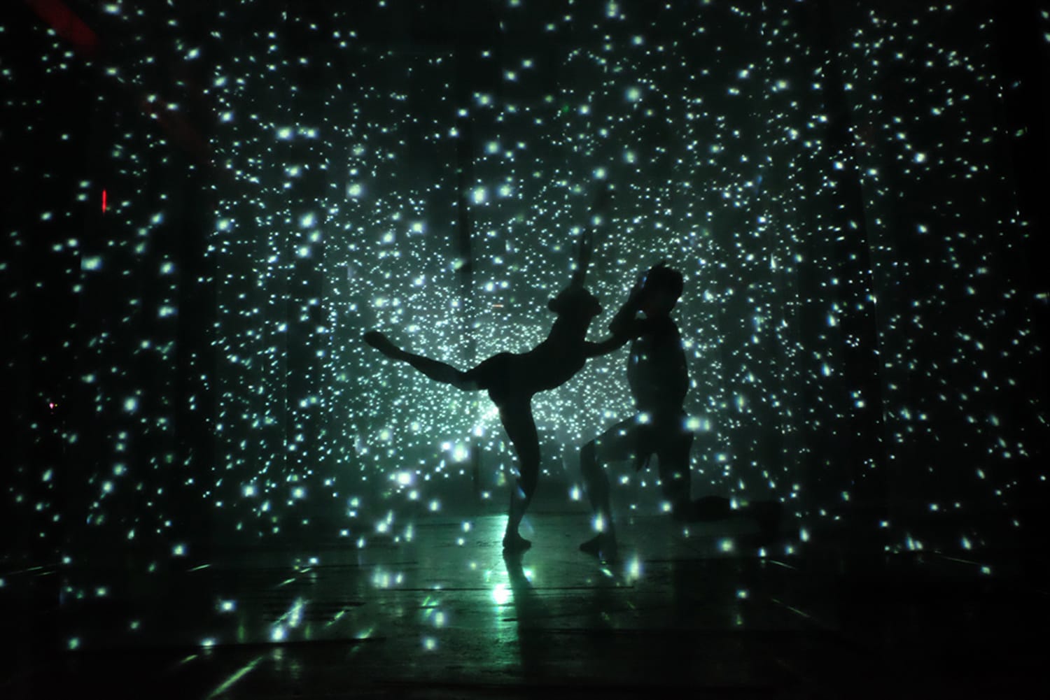 Silhouettes of dancers performing against a backdrop of glowing stars in a dark, cosmic setting.