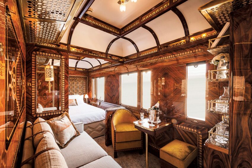 Luxurious vintage train carriage interior with elegant wood paneling, plush seating, a bed, and decorative lighting.