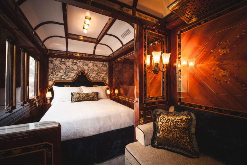 Luxurious vintage train cabin with ornate wood paneling, elegant decor, and a plush bed with decorative pillows.