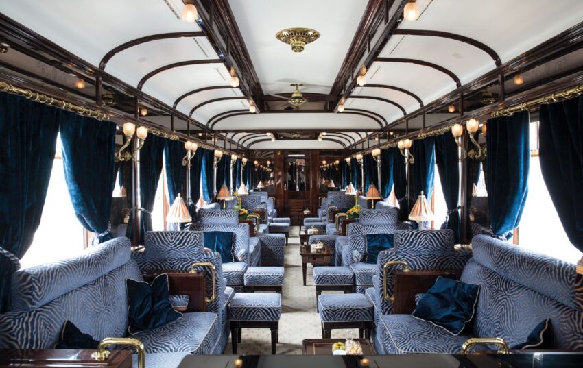 Luxurious vintage train interior with plush blue seating, elegant lighting, and rich wooden details.