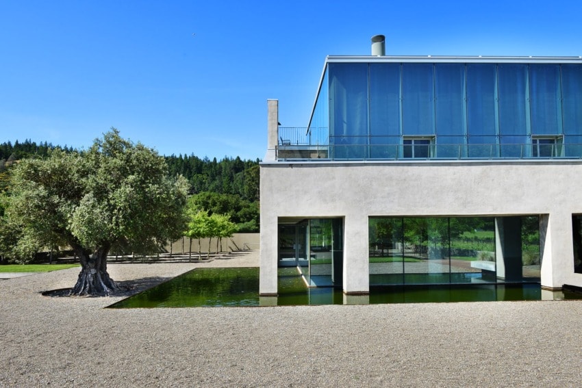 Modern building with large glass windows beside a reflecting pool, surrounded by trees and a clear blue sky.