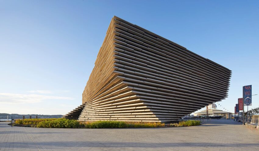 Modern architectural building with layered design against a clear blue sky and paved foreground.