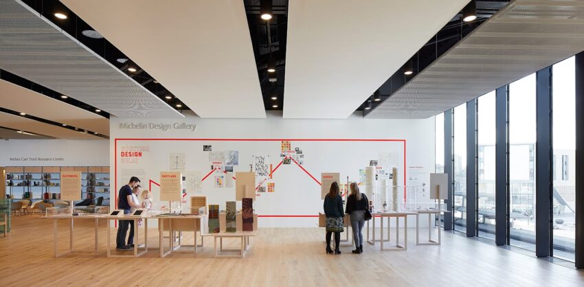People viewing exhibits in a modern design gallery with large windows and bright interior.