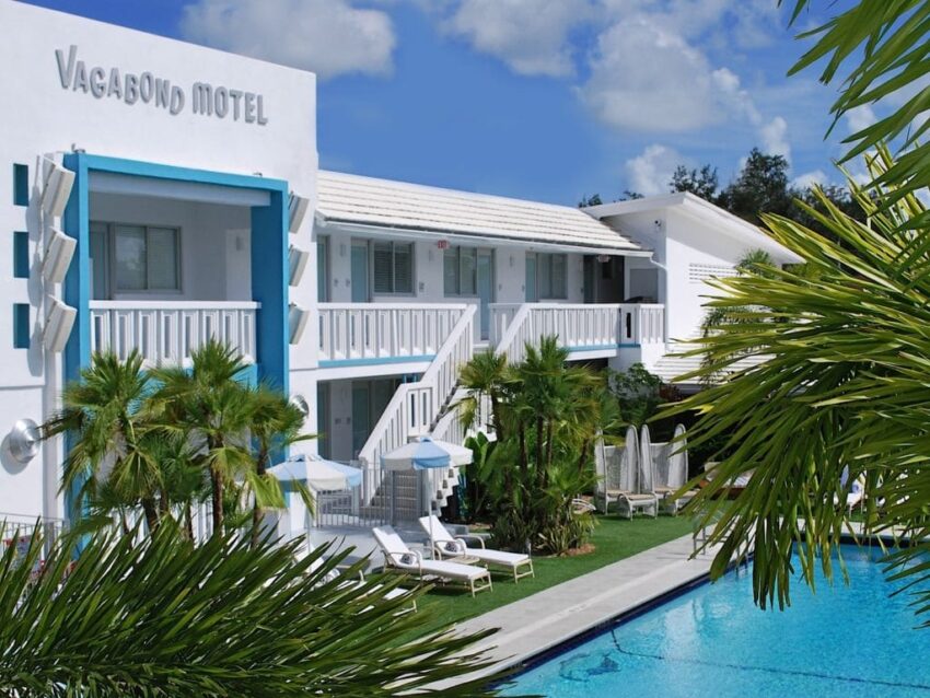 Retro-style motel with blue accents, palm trees, and pool under a clear sky.