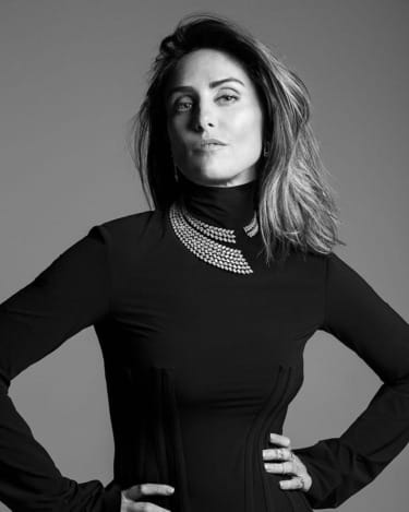 Woman posing confidently in black attire, adorned with a stylish necklace against a plain background.