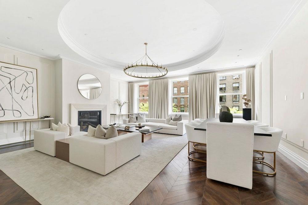 Spacious modern living room with white sofas, round chandelier, large windows, abstract art, and hardwood flooring.