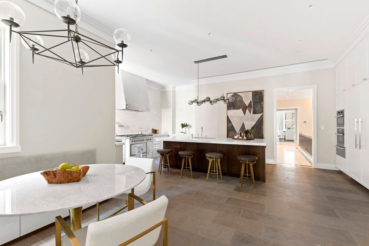 Modern kitchen with a marble dining table, bar stools at the island, stainless steel appliances, and contemporary art on the wall.