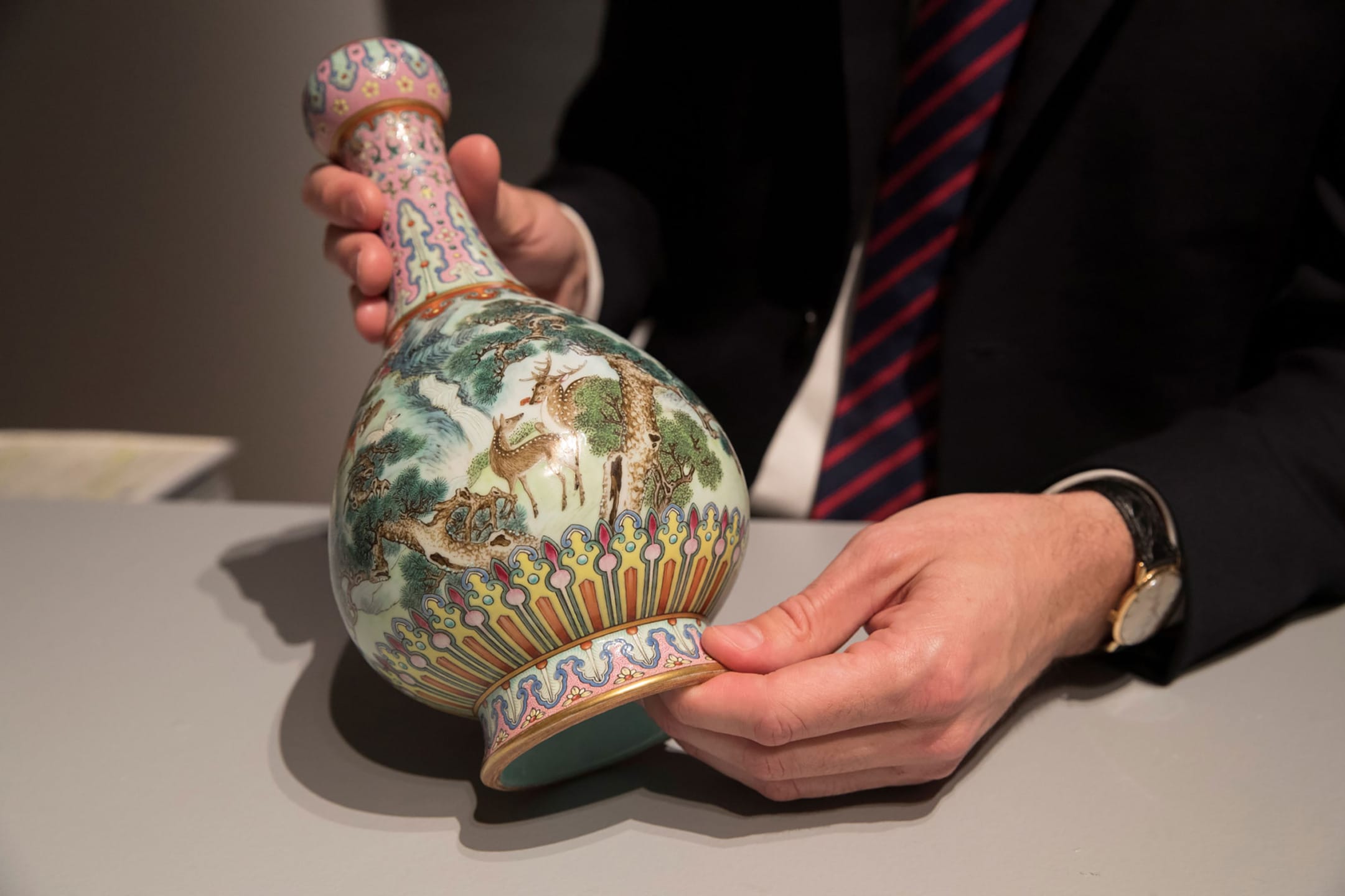 A person holding a decorative porcelain vase with intricate patterns and landscape painting.