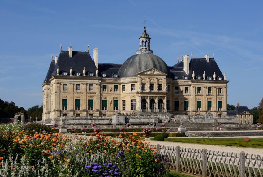 Baroque-style Vaux-le-Vicomte Chateau in France, front view with colorful garden in foreground.