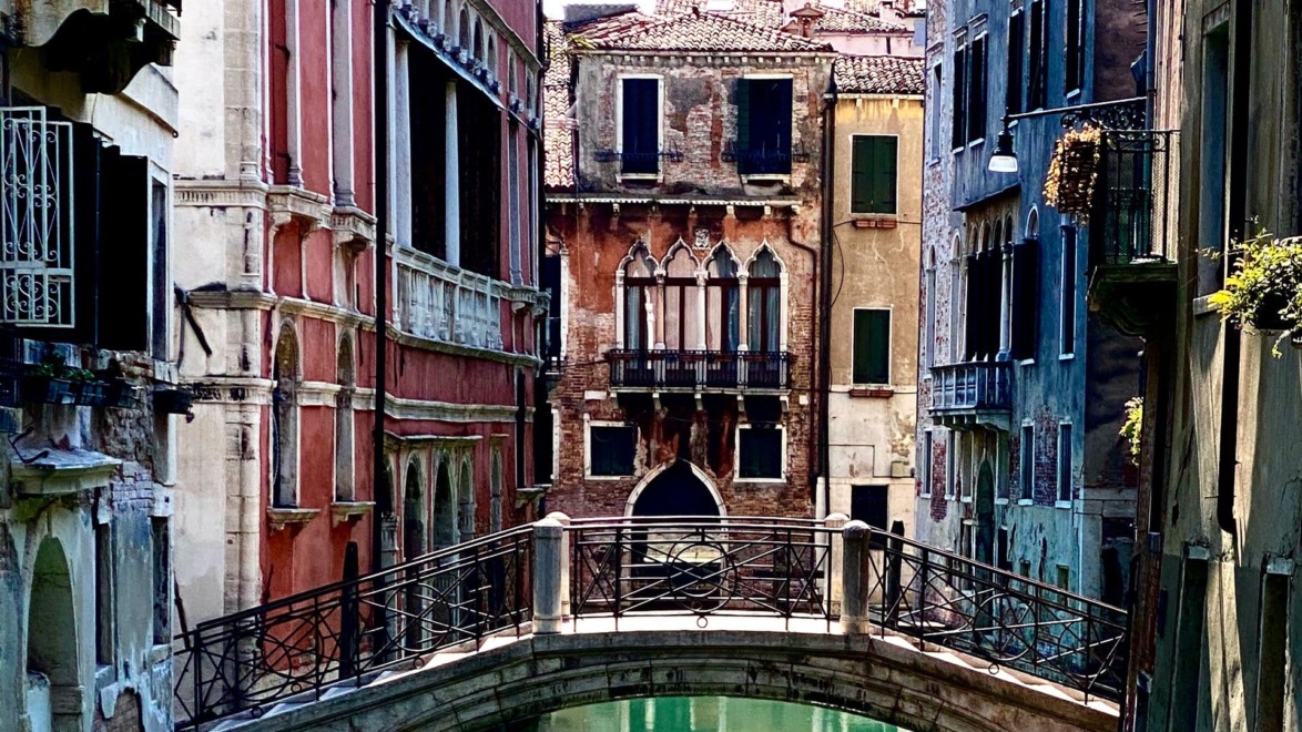 Scenic view of a Venetian canal with a stone bridge and colorful historic buildings in Venice, Italy.