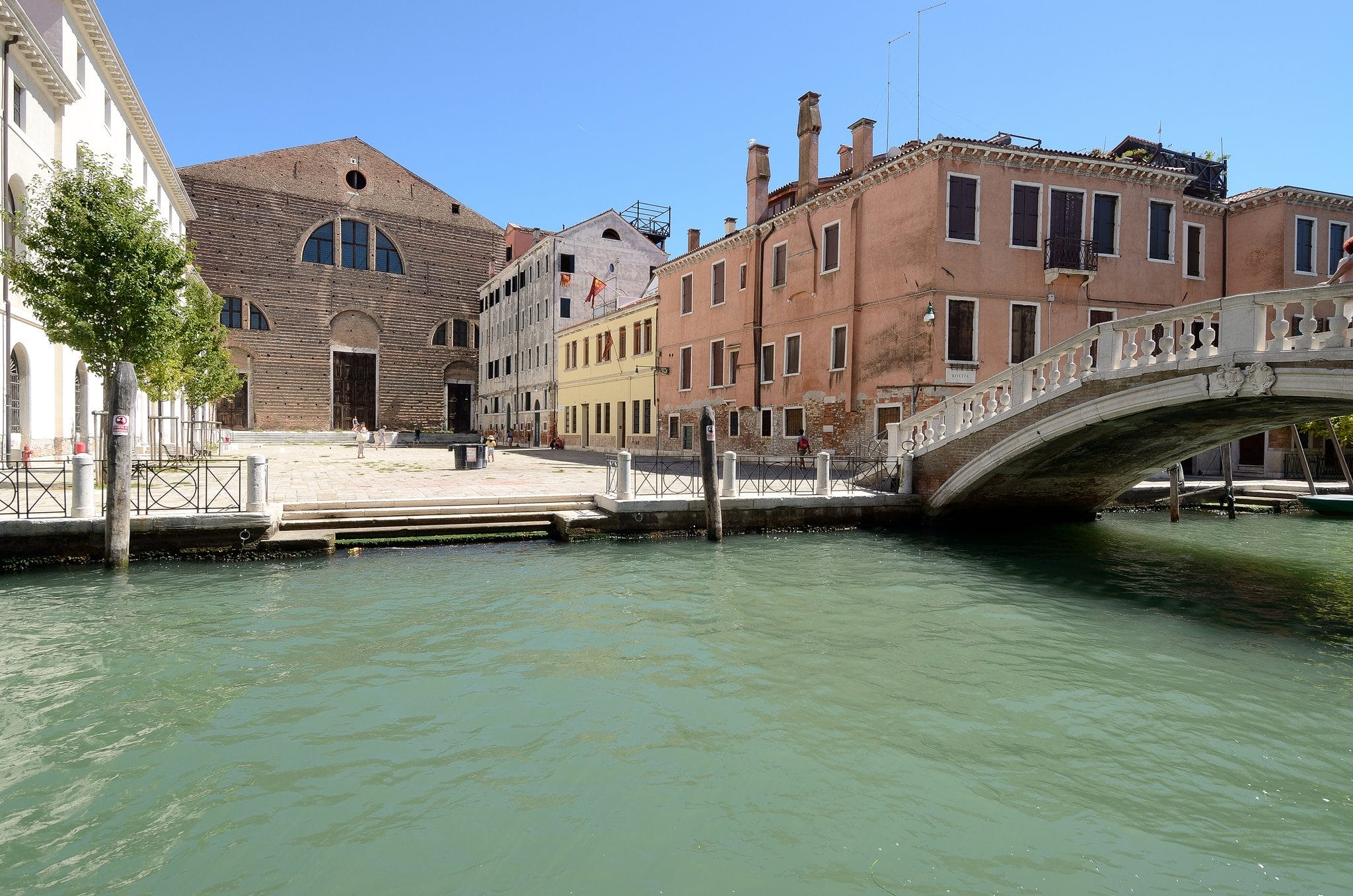 Venetian canal with historic buildings and a stone bridge under a clear blue sky.