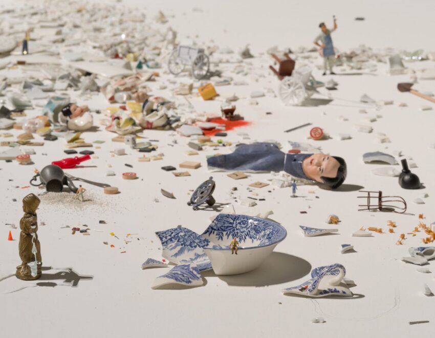 A broken ceramic bowl with blue patterns on a table surrounded by various miniature objects and debris.