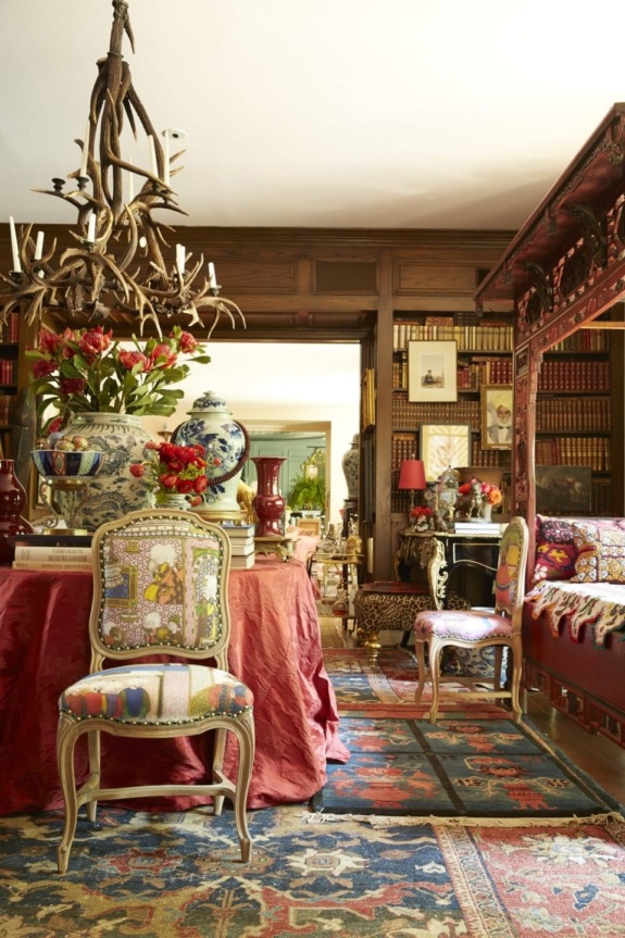 Eclectic living room with colorful chairs, vibrant rugs, antler chandelier, bookshelves, and ornate decor elements.