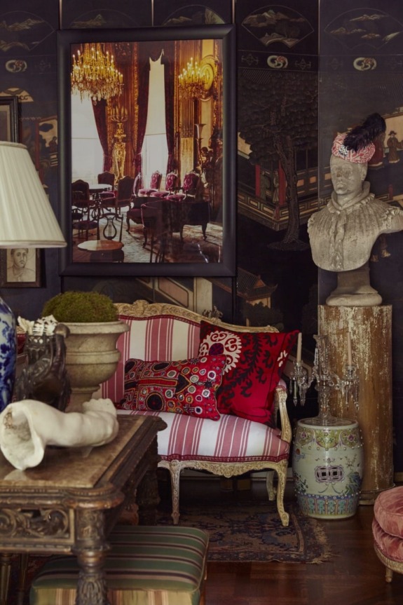 Eclectic vintage room with ornate furniture, vibrant pillows, a classical bust, and a large framed photo of an elegant dining room.