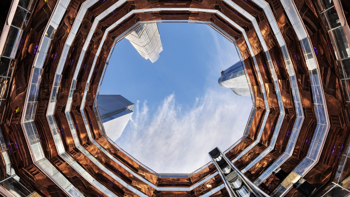 View looking up at the sky surrounded by the interior architecture of a modern, multi-story building with a unique design.