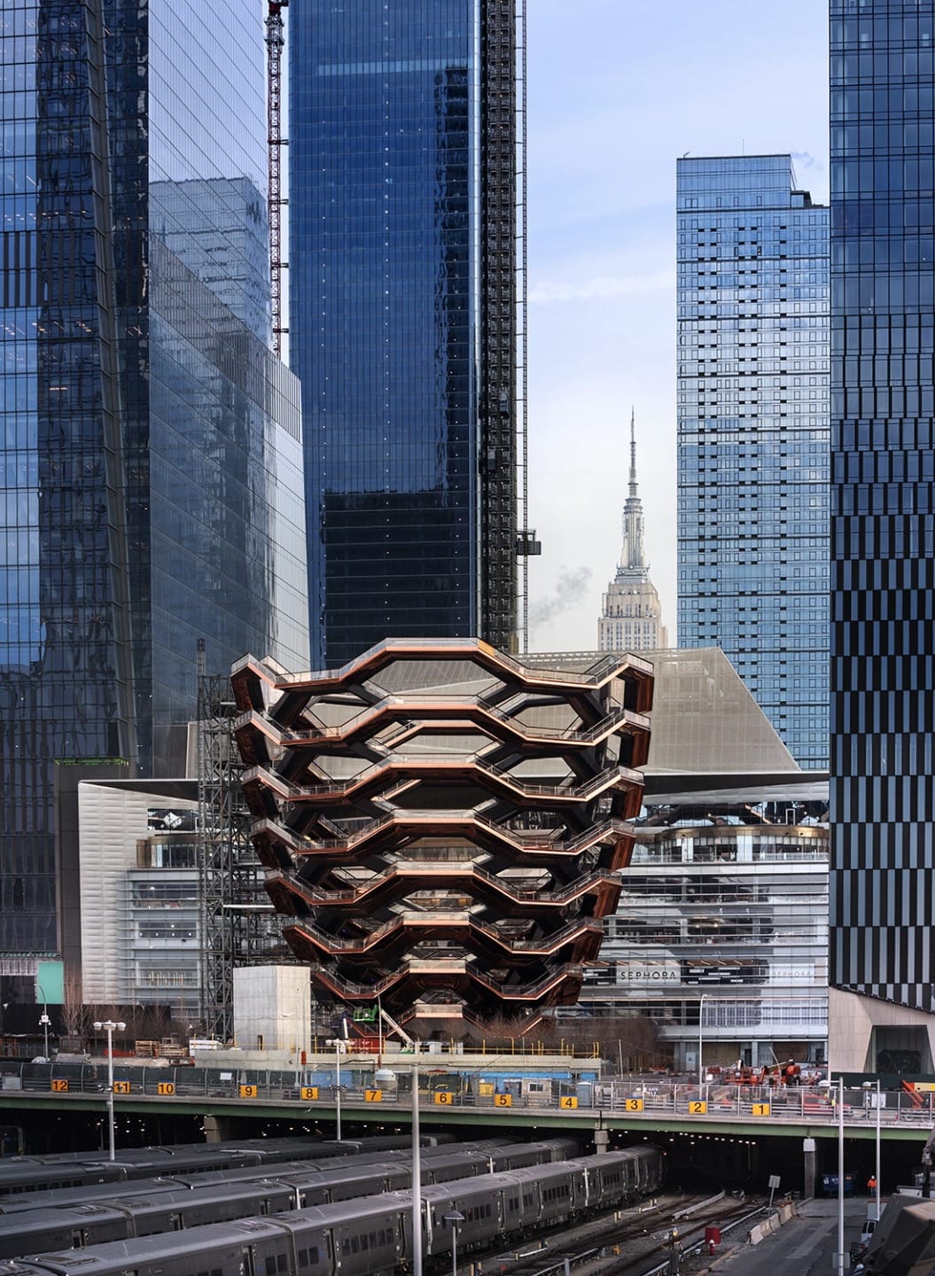 Vessel in Hudson Yards, New York City, surrounded by modern skyscrapers, with the Empire State Building visible in the distance.