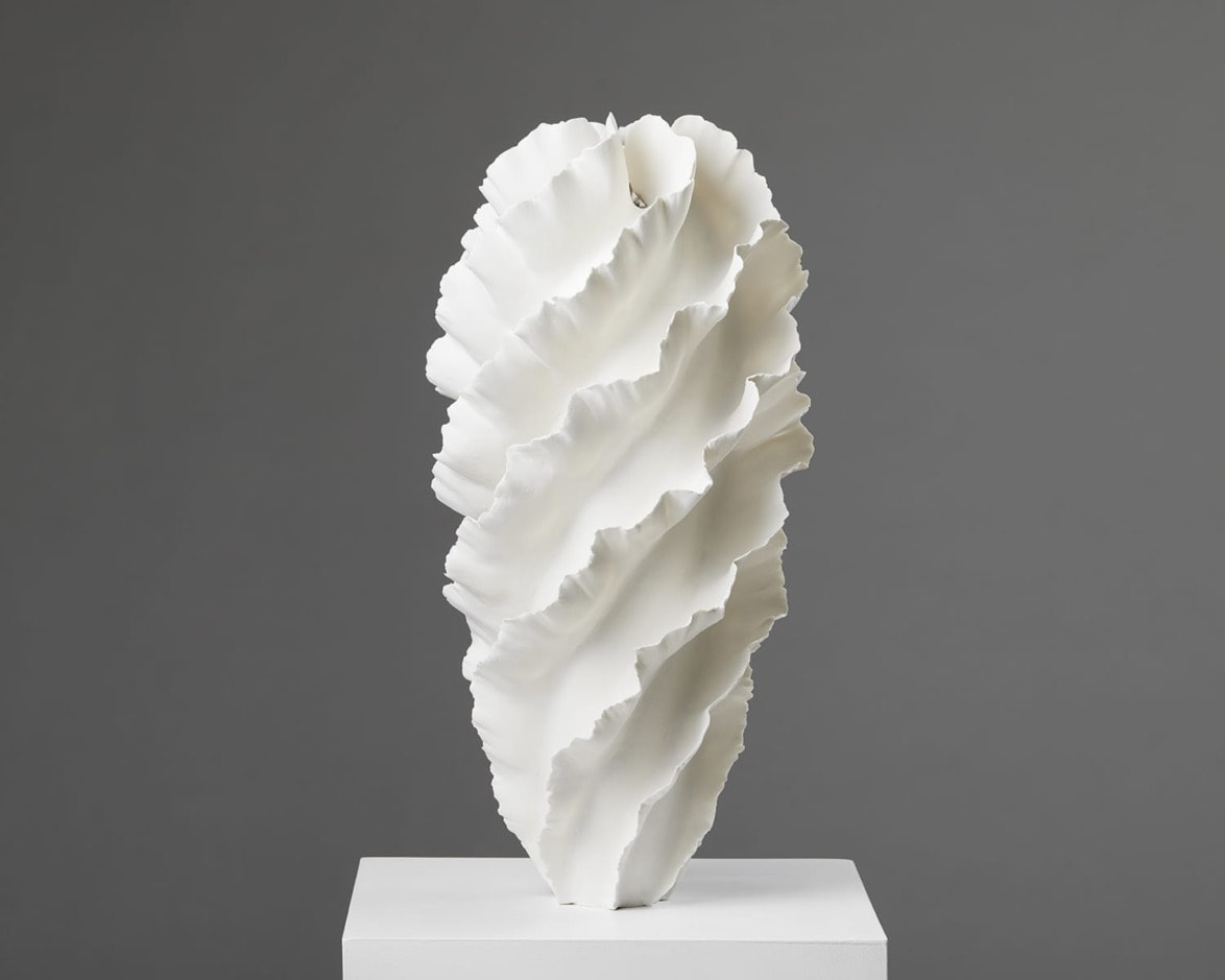 White abstract ceramic sculpture with textured, ruffled layers on a pedestal against a gray background.