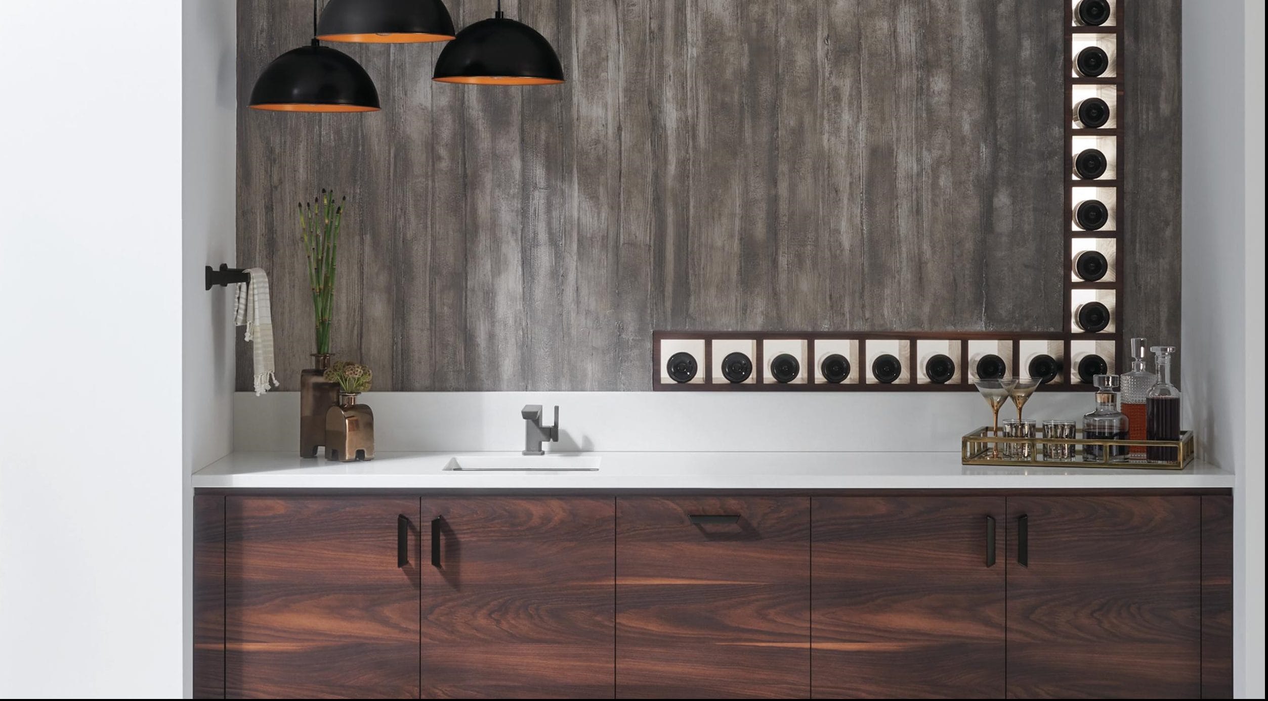 Modern kitchen with wood cabinets, white countertop, wall-mounted lighting, and decorative vases against a textured wall.
