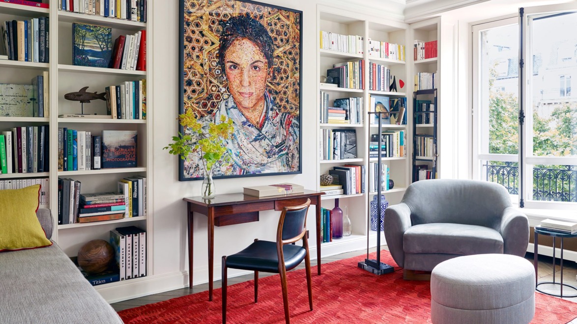 Cozy reading nook with armchair, desk, vibrant artwork, and bookshelves filled with books in a sunlit room.