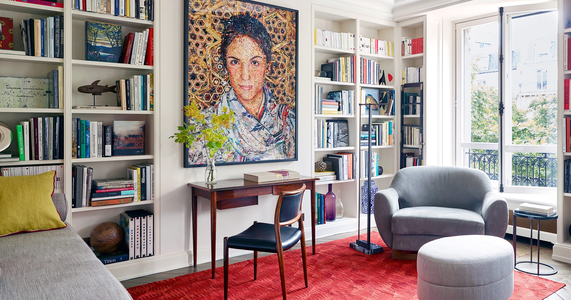 Cozy reading nook with armchair, desk, vibrant artwork, and bookshelves filled with books in a sunlit room.