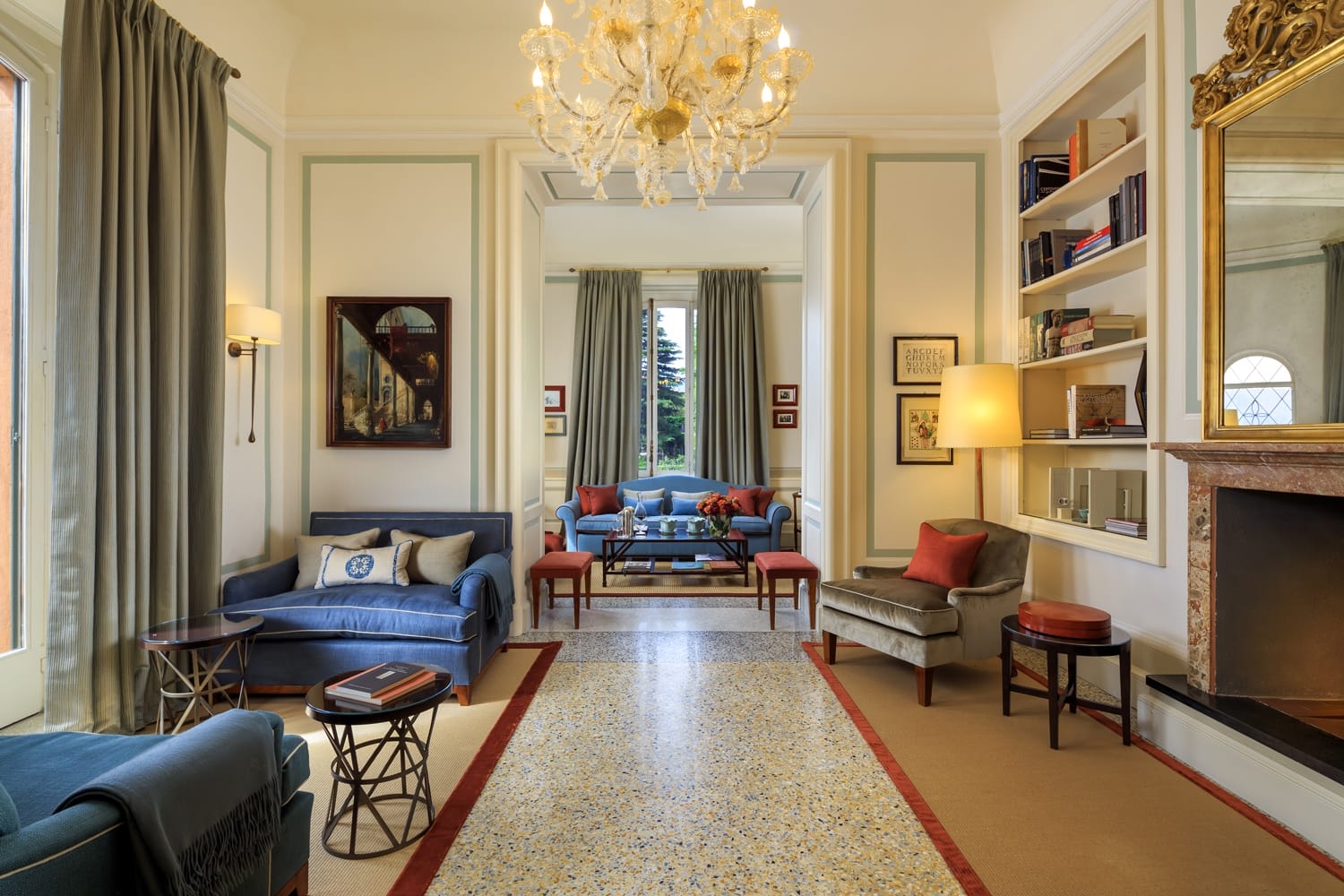 Elegant living room with chandelier, plush sofas, bookshelf, and large windows allowing natural light, creating a cozy ambiance.