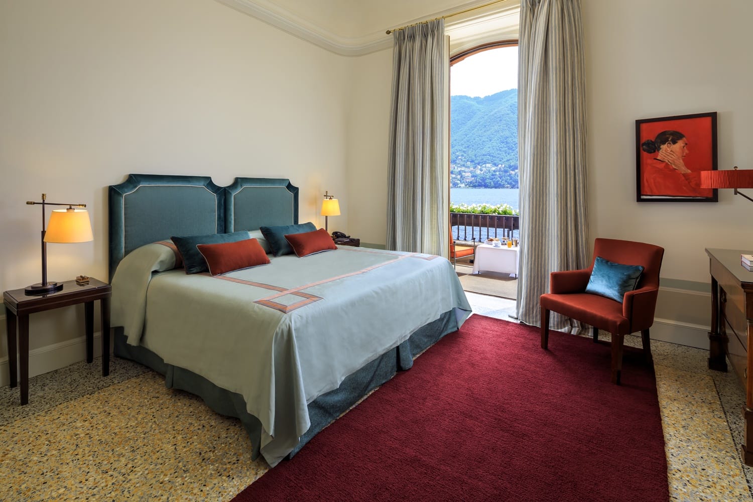 Luxury hotel room with a large bed, modern furniture, and a balcony view of mountains and a lake.