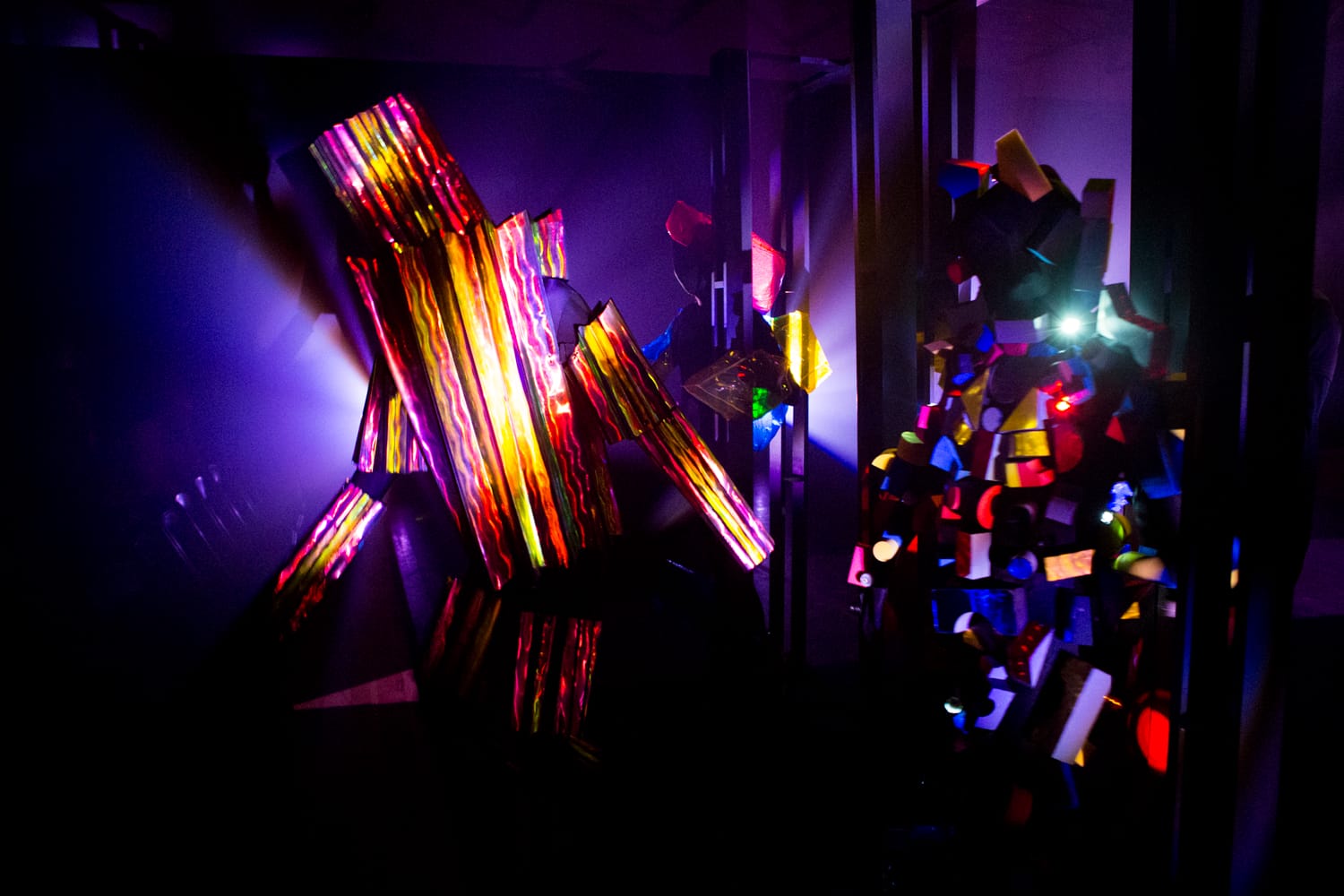 Colorful abstract art installation with various shapes illuminated by vibrant lights in a dark room.