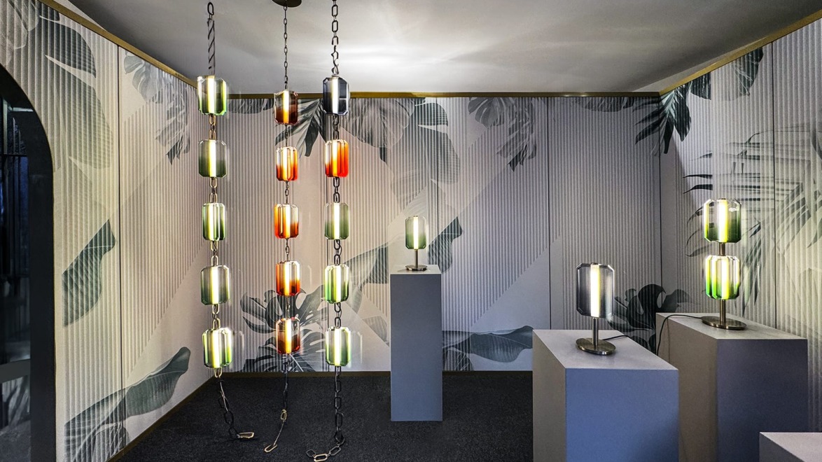 Modern lighting display with pendant and table lamps in a decorated room with leaf-patterned walls and dark flooring.
