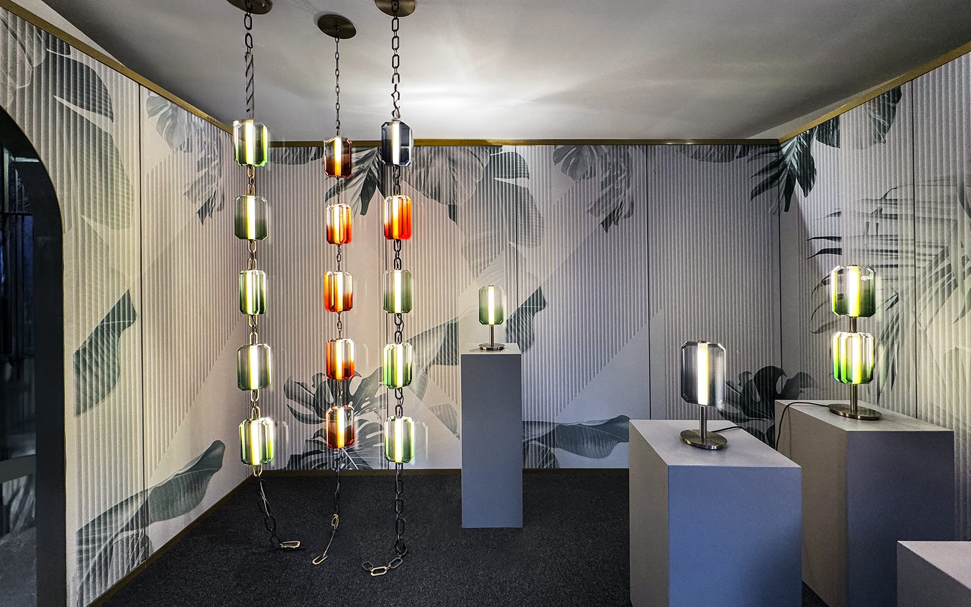 Modern lighting display with pendant and table lamps in a decorated room with leaf-patterned walls and dark flooring.