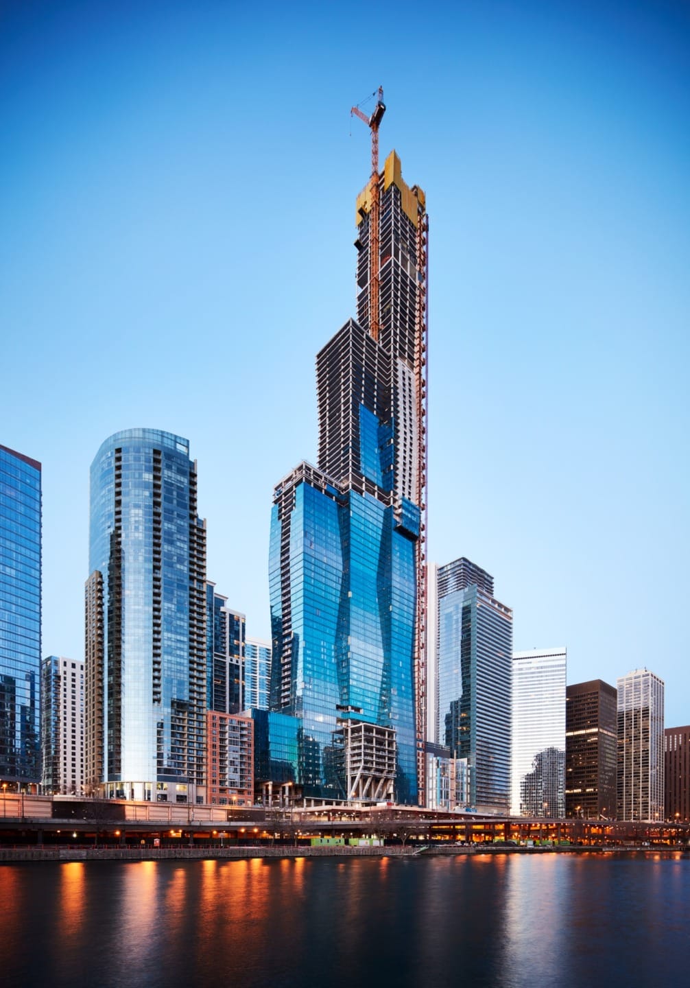 Chicago skyline with a modern skyscraper under construction, reflecting in a calm river at dusk.
