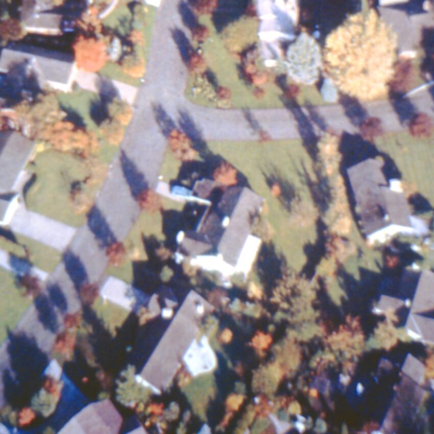 Aerial view of a suburban neighborhood with houses, trees, and winding roads on a sunny autumn day.