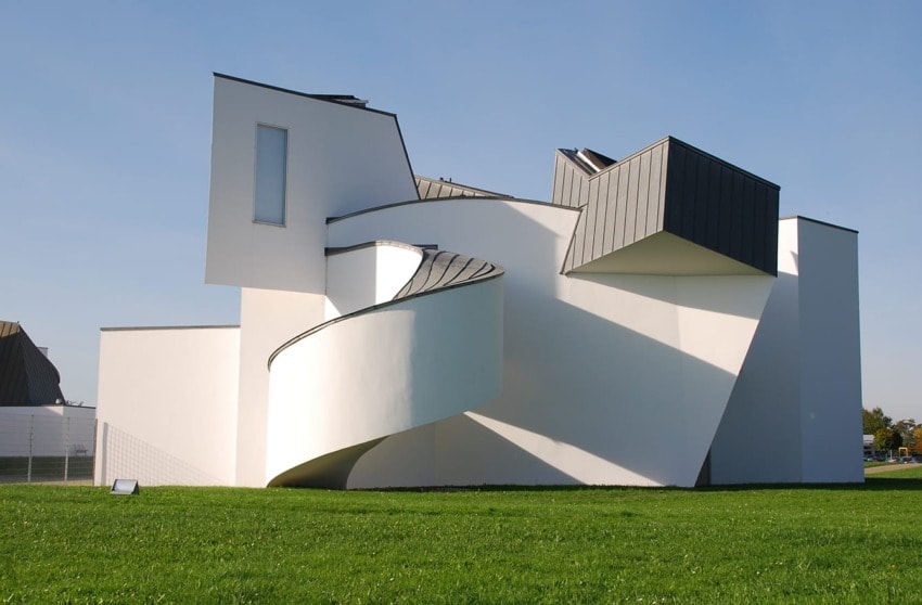 Modern white building with angular design and curved exterior staircase, set against a clear blue sky and green grass.