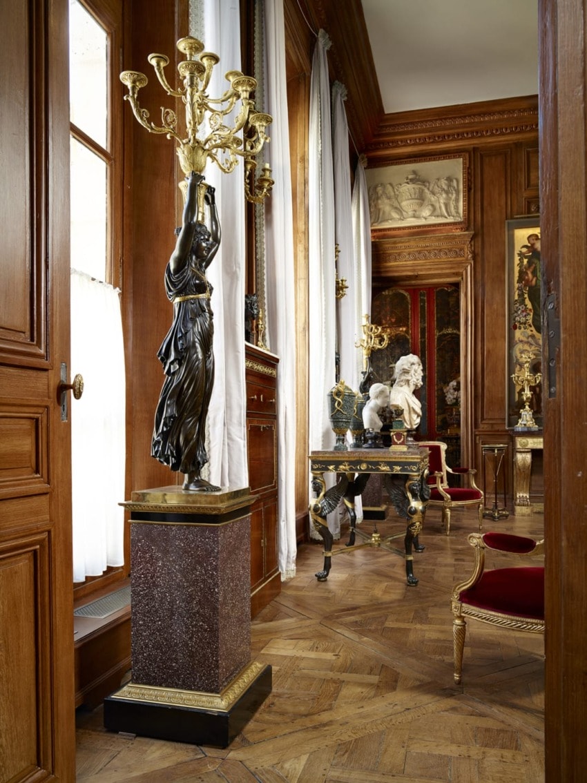 Luxurious room with wooden paneling, elegant sculptures, red velvet chairs, and a decorative chandelier.