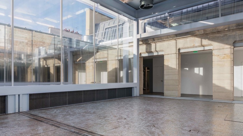 Sunlit modern interior with glass walls, high ceilings, and stone accents, showcasing a blend of industrial and classic design.