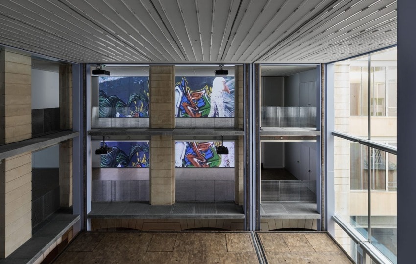 Interior view of a modern building with colorful mural art on the walls and large glass windows.