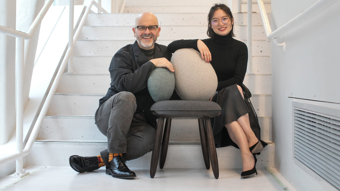 Two people sitting on stairs with a uniquely designed chair between them, featuring round seat and back cushions.