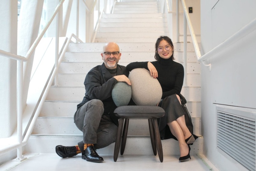 Two people sitting on a staircase with two cushioned chairs, smiling and posing for the photo.