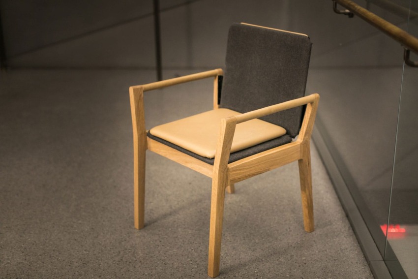 Wooden chair with gray backrest and beige seat cushion, placed on a gray floor next to a glass railing.