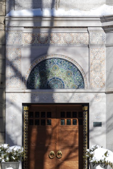 Ornate wooden door with decorative mosaic arch and snow-covered surroundings.