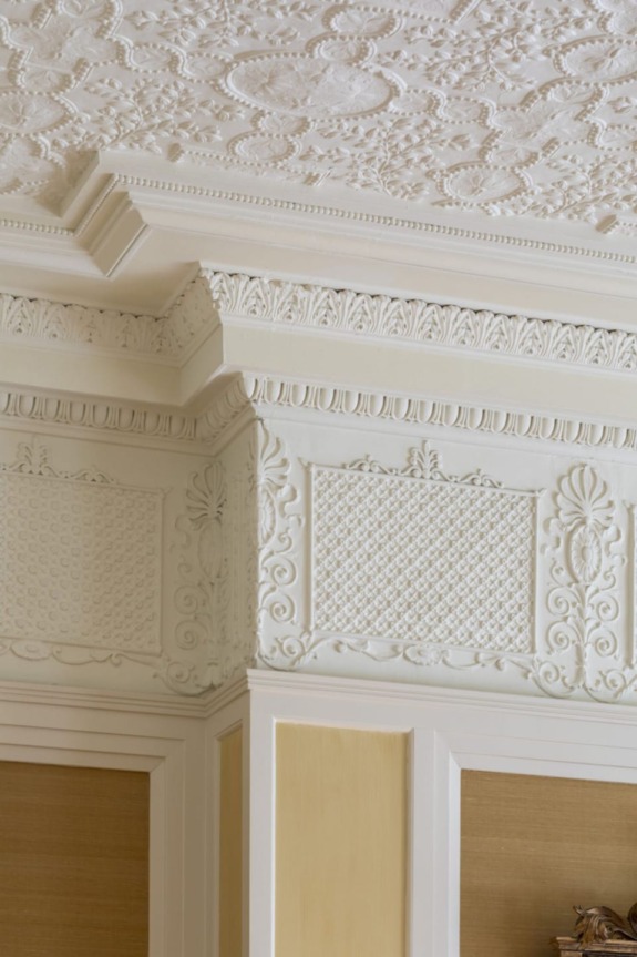 Ornate white plaster ceiling and wall corner with intricate decorative patterns and molding details.