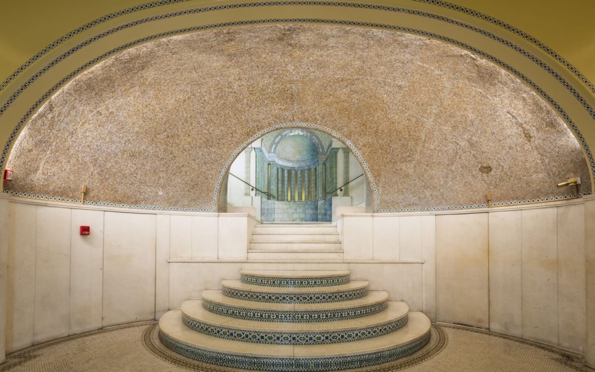Elegant, curved staircase leading to a tiled archway, adorned with intricate mosaic details and warm, ambient lighting.