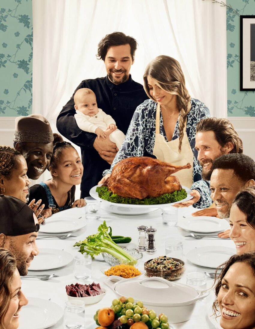Family gathered around a table with a roasted turkey centerpiece, smiling and enjoying a festive meal together.