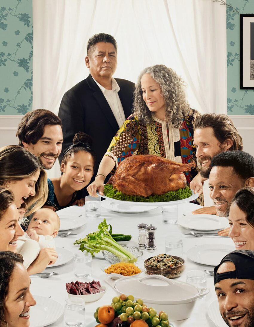 A diverse group of people around a table, eagerly looking at a large roasted turkey centerpiece.