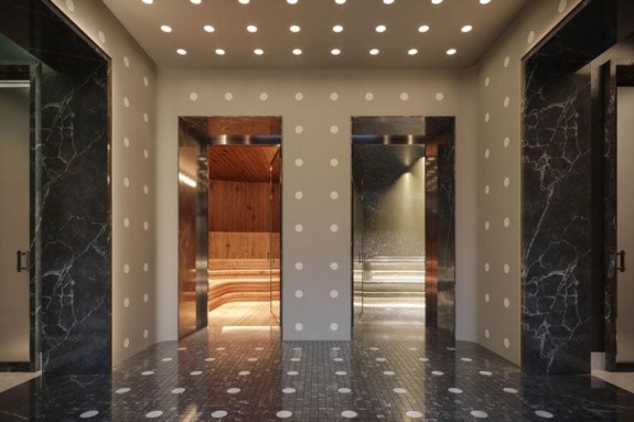 Modern elevator lobby with marble floors and walls, featuring three illuminated elevator doors and a ceiling with circular lights.