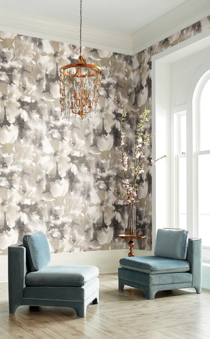 Elegant living room with two blue chairs, floral arrangement, abstract wallpaper, wooden floor, and a decorative chandelier.