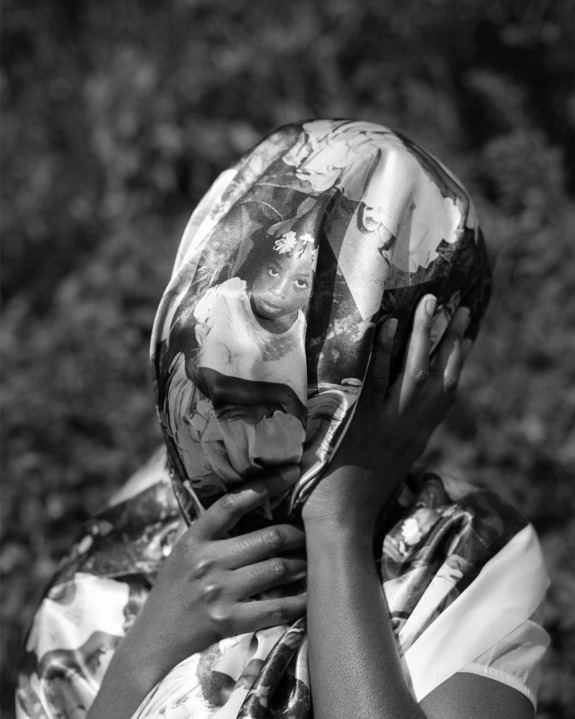 Person holding fabric printed with photo of a child, covering their face, in black and white, with a blurred background.