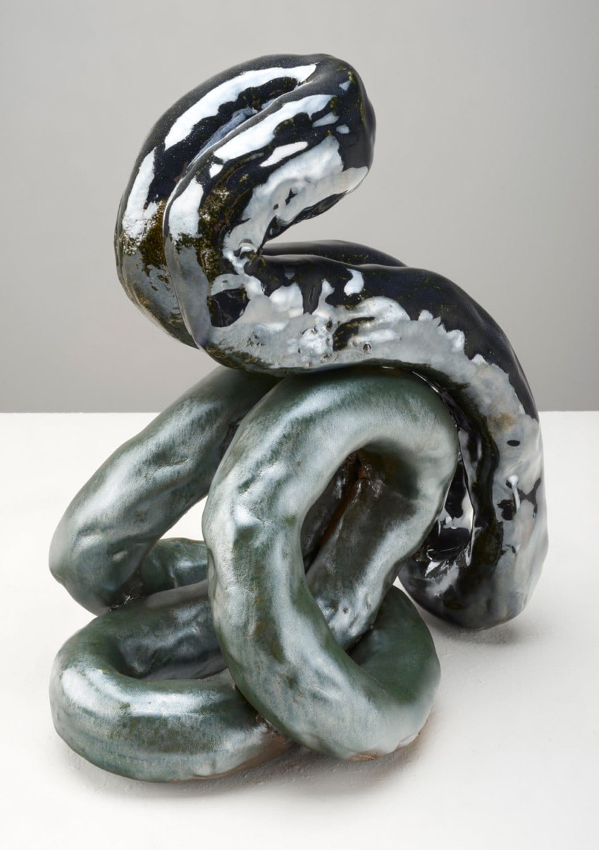 Abstract ceramic sculpture with intertwining glossy, black and greenish shapes on a white background.