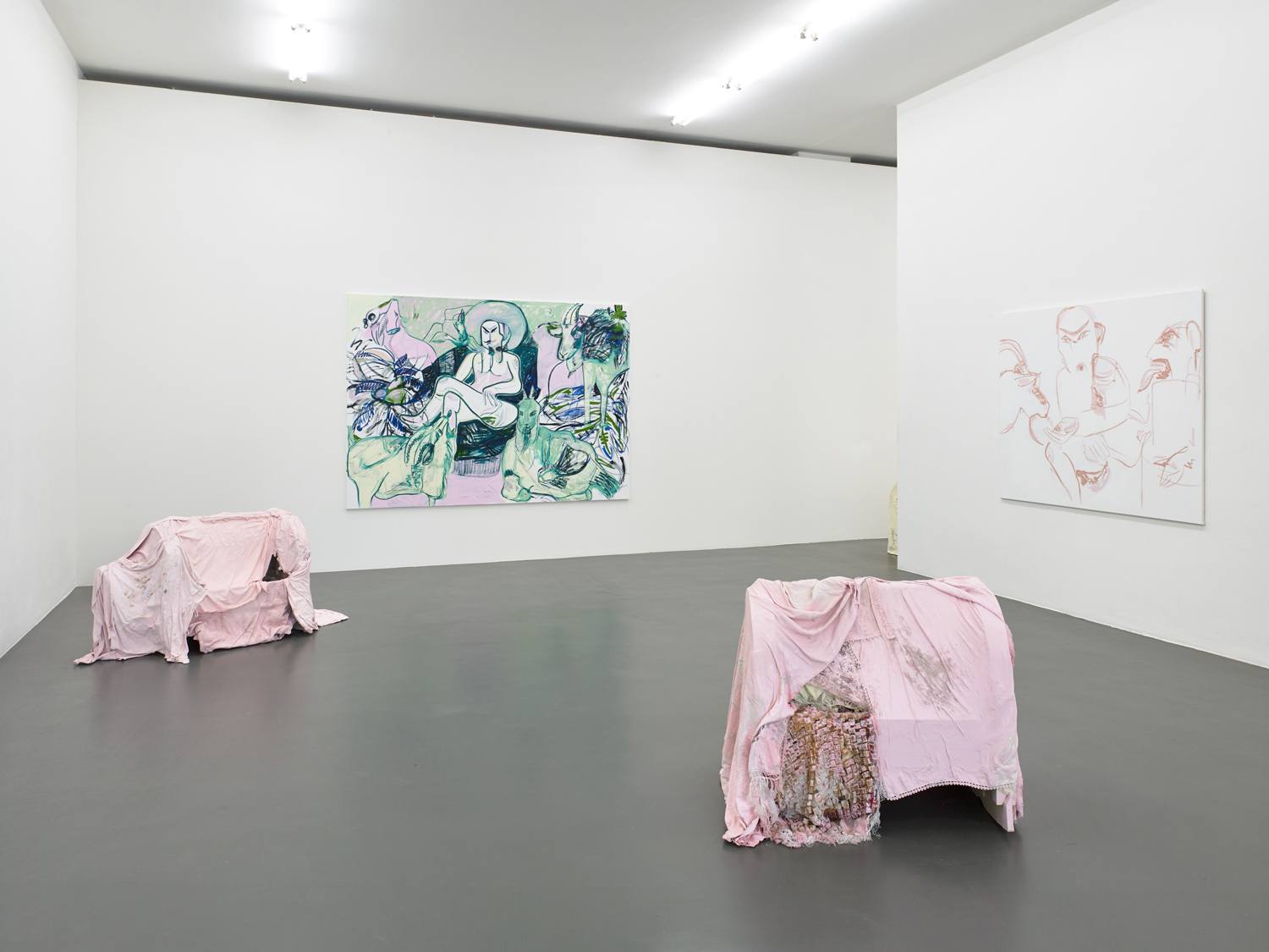Art gallery room with abstract paintings on walls and installations covered with pink fabric on the floor.