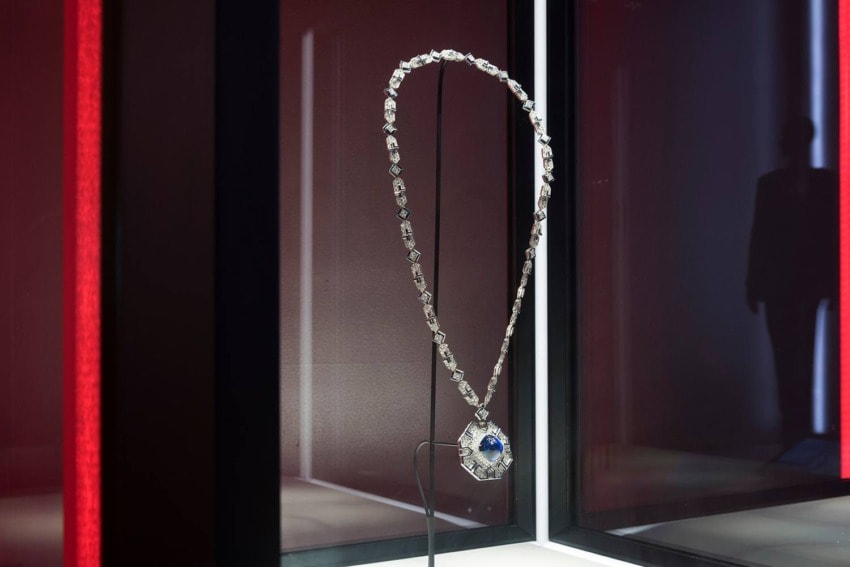 Elegant necklace with diamond-studded chain and blue gemstone pendant displayed against a dark, modern background.