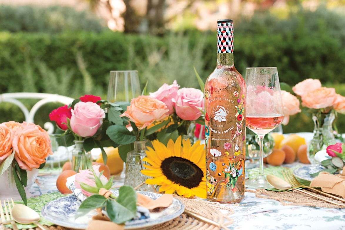 Colorful outdoor table setting with flowers, a decorative bottle of rosé wine, and filled wine glasses.